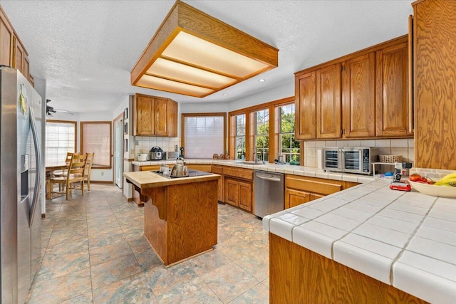 kitchen with a kitchen island, tasteful backsplash, tile counters, kitchen peninsula, and stainless steel appliances