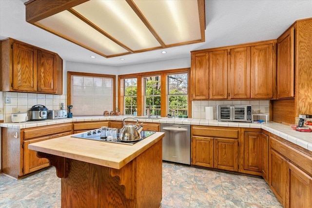 kitchen with tile counters, a kitchen island, black electric cooktop, decorative backsplash, and stainless steel dishwasher