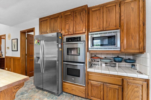 kitchen featuring stainless steel appliances, tile counters, backsplash, and a textured ceiling