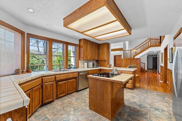 kitchen featuring sink, tile countertops, a center island, a textured ceiling, and stainless steel appliances