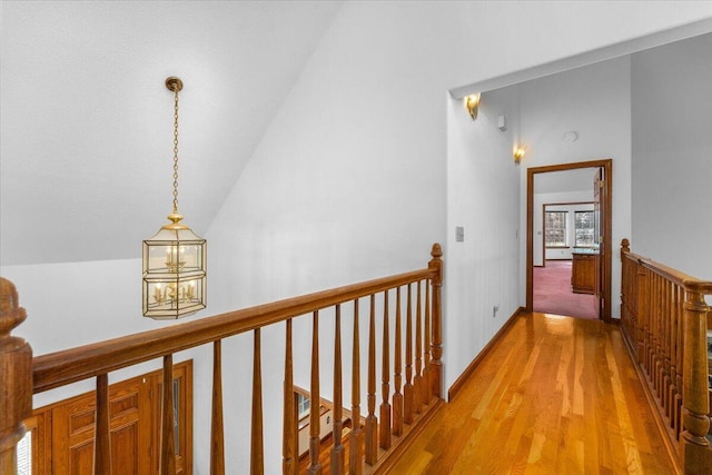 corridor with lofted ceiling, wood-type flooring, and a notable chandelier