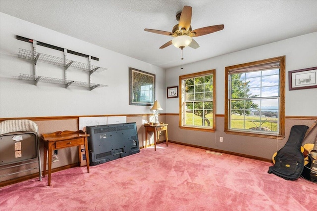 living area featuring ceiling fan, carpet floors, and a textured ceiling