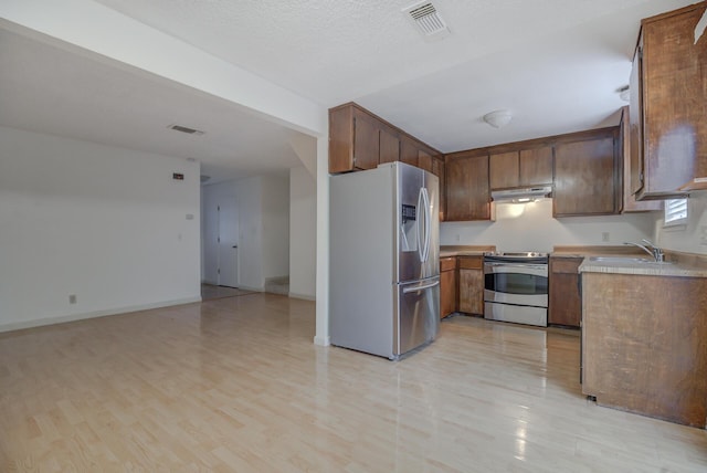 kitchen featuring stainless steel appliances, sink, a textured ceiling, and light hardwood / wood-style floors