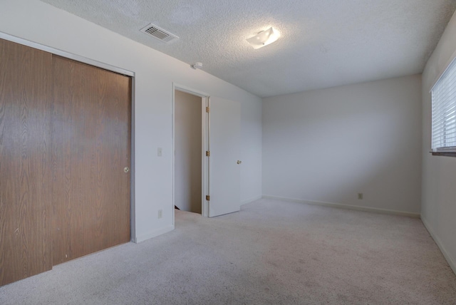 unfurnished bedroom with light carpet, a textured ceiling, and a closet