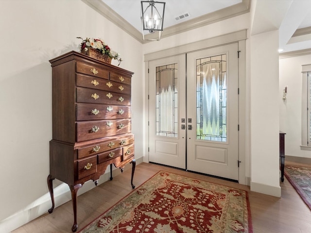 entryway with ornamental molding, a chandelier, light hardwood / wood-style floors, and french doors