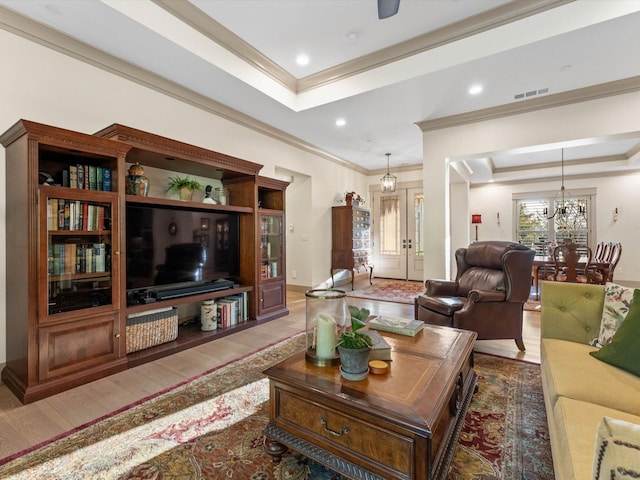 living room featuring hardwood / wood-style flooring, ornamental molding, an inviting chandelier, and a tray ceiling