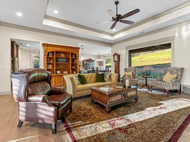 living room with crown molding, a tray ceiling, ceiling fan with notable chandelier, and hardwood / wood-style flooring