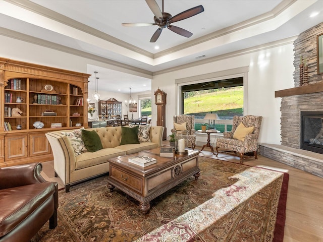 living room with ceiling fan with notable chandelier, a fireplace, ornamental molding, a raised ceiling, and dark wood-type flooring