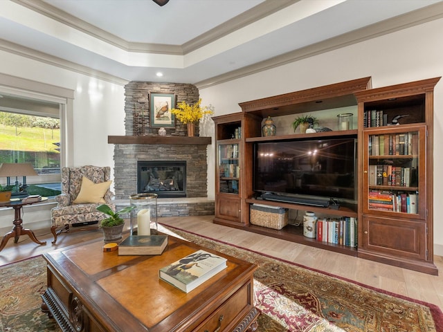 living room featuring a tray ceiling, ornamental molding, a fireplace, and light hardwood / wood-style flooring