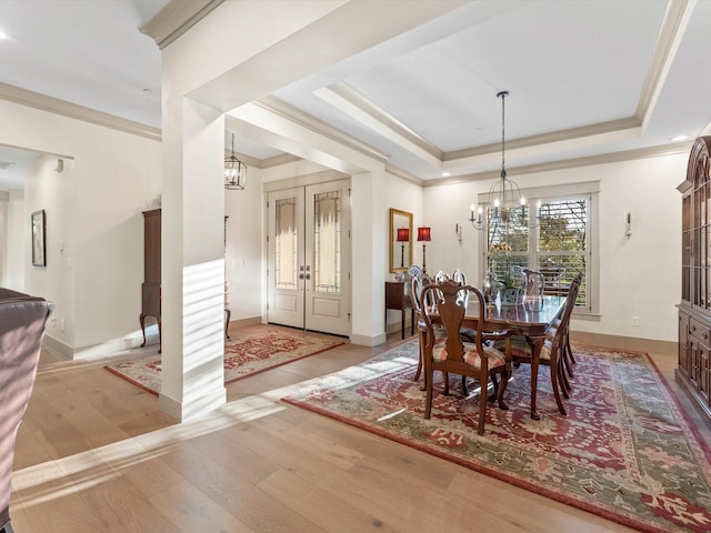 dining room featuring an inviting chandelier, ornamental molding, a raised ceiling, and light hardwood / wood-style flooring