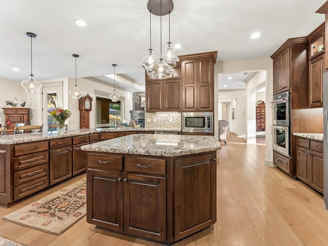 kitchen with a center island, light hardwood / wood-style flooring, appliances with stainless steel finishes, pendant lighting, and backsplash