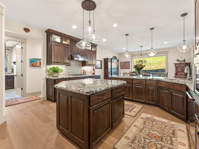 kitchen with pendant lighting, decorative backsplash, a center island, light stone counters, and dark brown cabinetry