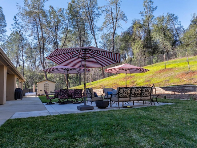 view of community featuring a yard, a patio area, an outdoor living space with a fire pit, and a storage unit