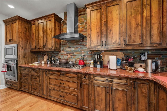 kitchen featuring stone counters, appliances with stainless steel finishes, backsplash, light hardwood / wood-style floors, and wall chimney range hood