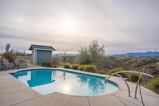 view of swimming pool featuring a mountain view, a patio area, and a storage shed