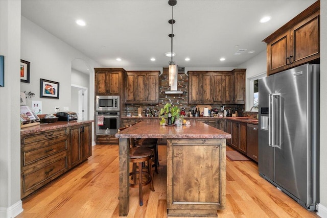 kitchen featuring hanging light fixtures, stainless steel appliances, tasteful backsplash, a kitchen island, and wall chimney exhaust hood