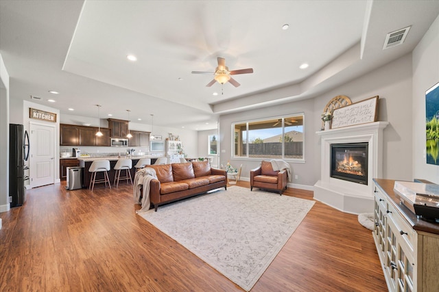 living room featuring dark wood-type flooring, ceiling fan, and a tray ceiling