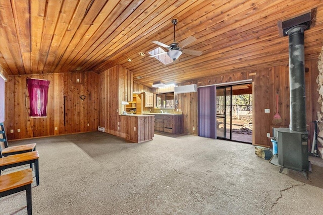 unfurnished living room with wood ceiling, wooden walls, ceiling fan, and a wood stove