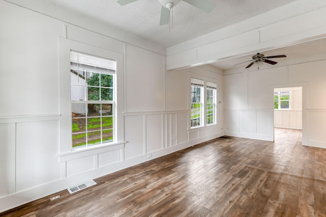 unfurnished room featuring a textured ceiling, visible vents, a decorative wall, and wood finished floors