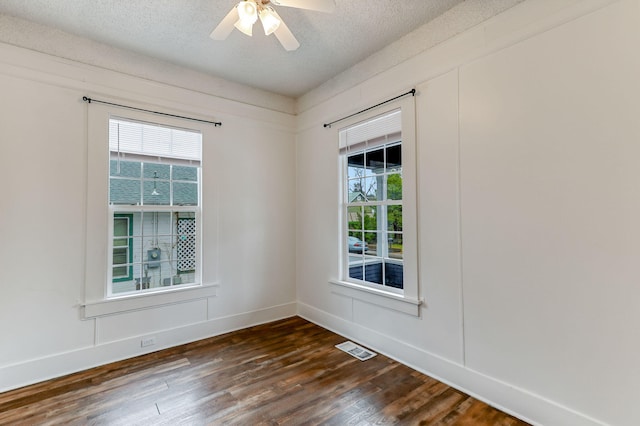 unfurnished room featuring a textured ceiling, dark wood-type flooring, visible vents, and a wealth of natural light