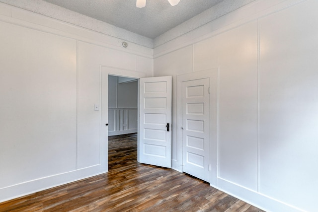 unfurnished room with a textured ceiling, a ceiling fan, a decorative wall, and dark wood-style flooring