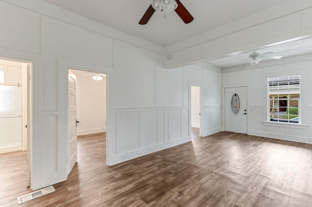 empty room featuring ceiling fan, visible vents, a decorative wall, and wood finished floors