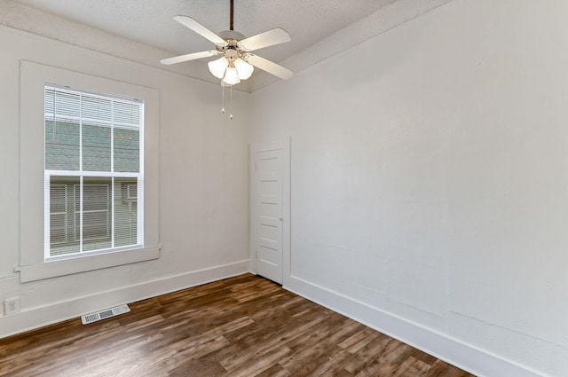 empty room featuring a textured ceiling, dark wood-style flooring, a ceiling fan, visible vents, and baseboards