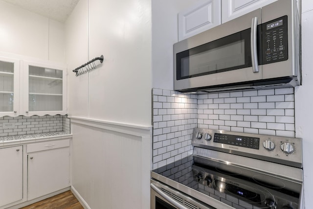 kitchen with stainless steel appliances, decorative backsplash, glass insert cabinets, white cabinetry, and wood finished floors