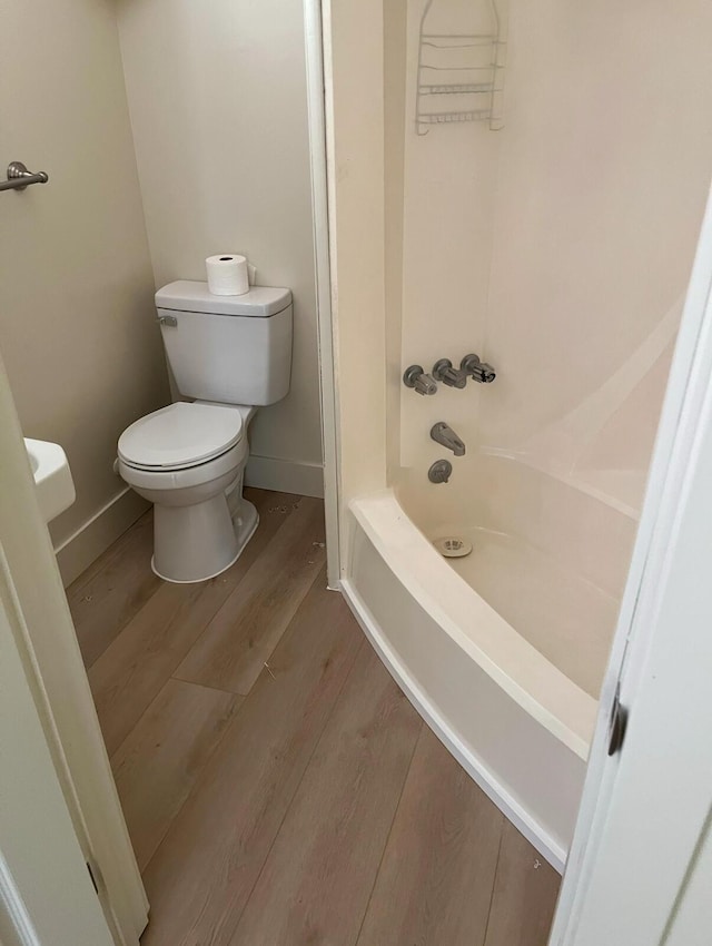 bathroom featuring tub / shower combination, wood finished floors, toilet, and baseboards