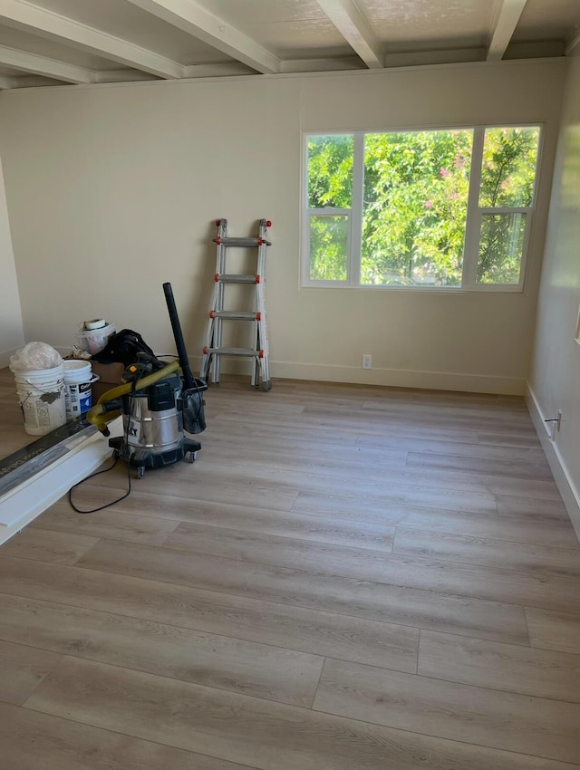 spare room with beamed ceiling, light wood-style flooring, and baseboards