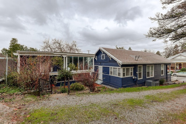 view of front of home featuring roof with shingles, central air condition unit, a sunroom, fence, and driveway