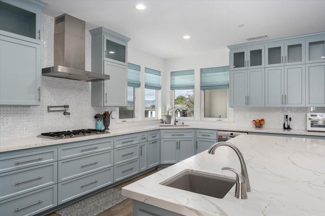 kitchen with light stone counters, wall chimney range hood, sink, and stainless steel gas cooktop