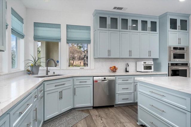 kitchen featuring sink, appliances with stainless steel finishes, dark hardwood / wood-style floors, light stone countertops, and decorative backsplash