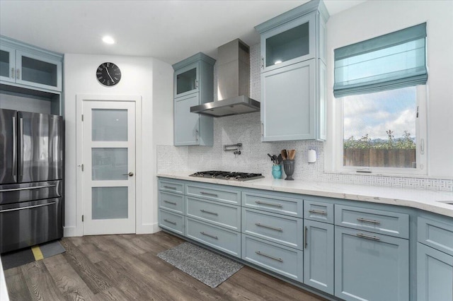 kitchen featuring wall chimney exhaust hood, light stone counters, tasteful backsplash, dark hardwood / wood-style flooring, and stainless steel appliances