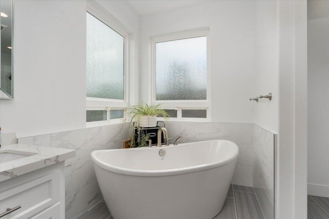 bathroom featuring vanity, a tub to relax in, and tile walls