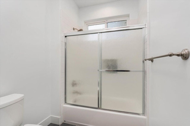 bathroom featuring combined bath / shower with glass door and toilet