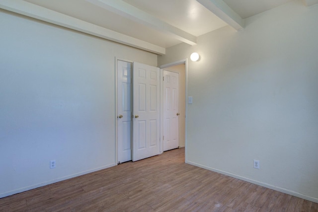 spare room with beamed ceiling and light hardwood / wood-style flooring