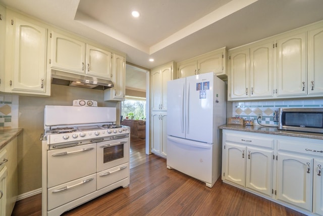 kitchen featuring dark wood-type flooring, white cabinetry, a raised ceiling, white appliances, and decorative backsplash