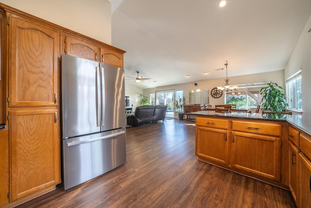 kitchen with open floor plan, hanging light fixtures, freestanding refrigerator, brown cabinets, and dark countertops