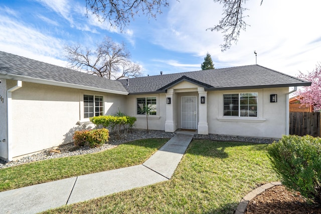 ranch-style home with a shingled roof, a front yard, fence, and stucco siding