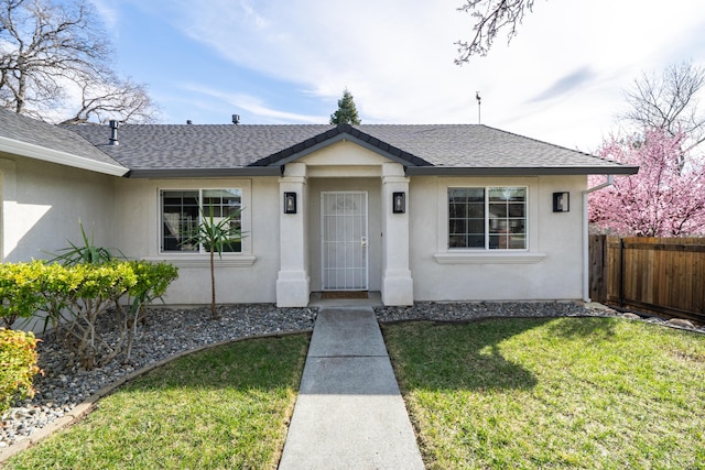 view of front of property with roof with shingles, fence, a front lawn, and stucco siding