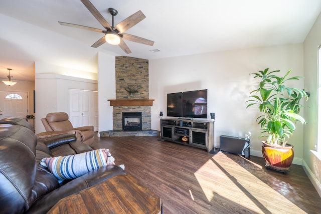 living room featuring dark wood-style flooring, lofted ceiling, ceiling fan, a stone fireplace, and baseboards