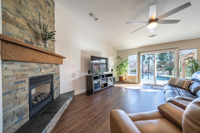 living room with dark wood-style floors, high vaulted ceiling, a stone fireplace, and visible vents