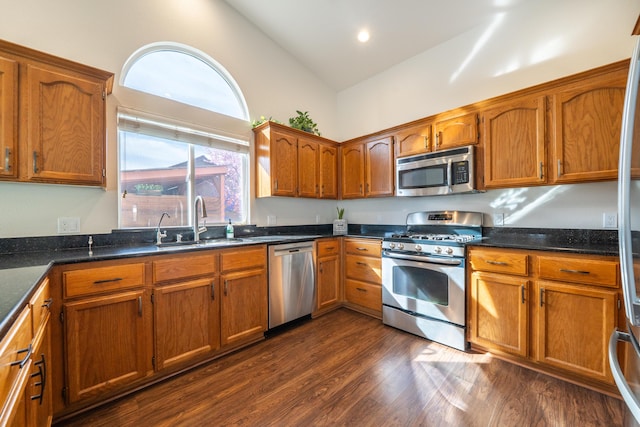 kitchen with stainless steel appliances, a sink, vaulted ceiling, brown cabinets, and dark wood finished floors