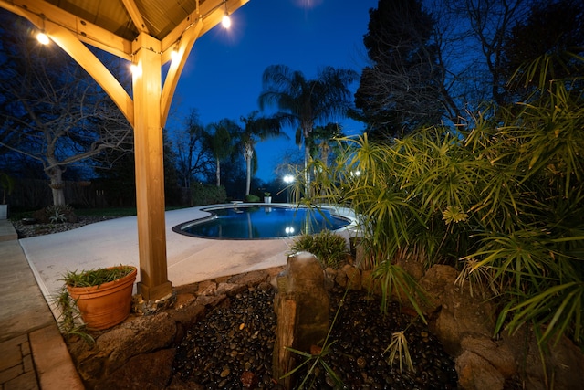 pool at night featuring a patio area and an outdoor pool