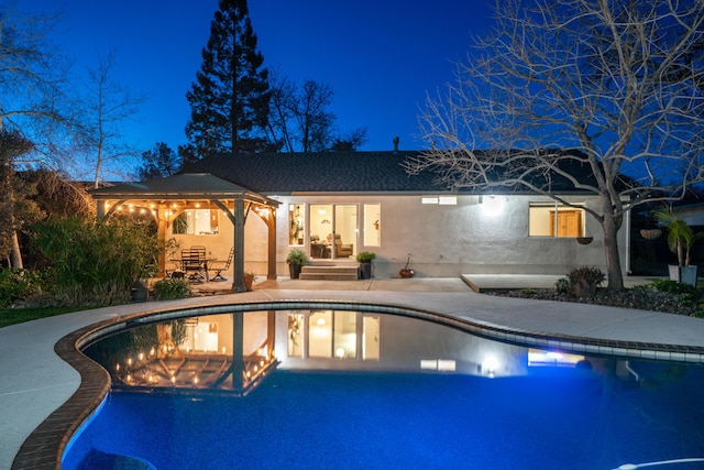 pool at night with a patio area, an outdoor pool, and a gazebo