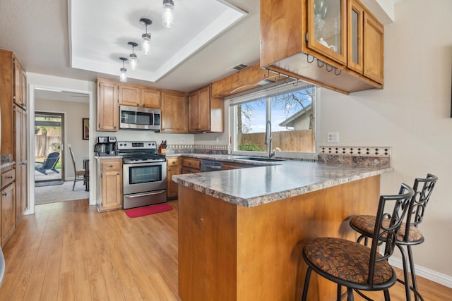 kitchen with stainless steel appliances, a breakfast bar area, kitchen peninsula, and a tray ceiling