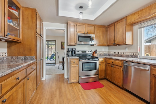 kitchen with hanging light fixtures, stainless steel appliances, light stone counters, a tray ceiling, and light wood-type flooring