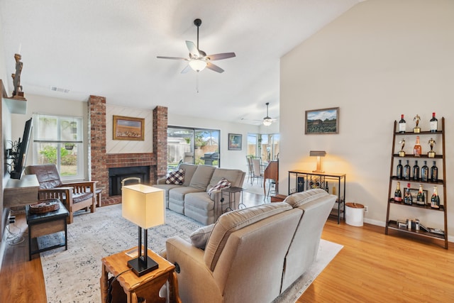 living room with ceiling fan, lofted ceiling, light hardwood / wood-style floors, and a brick fireplace