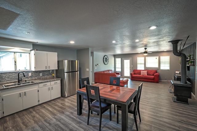 dining area featuring a wood stove, sink, a textured ceiling, and dark wood-type flooring